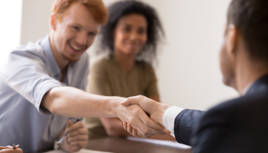 Two men are shaking hands while a female is sitting at the back smiling.